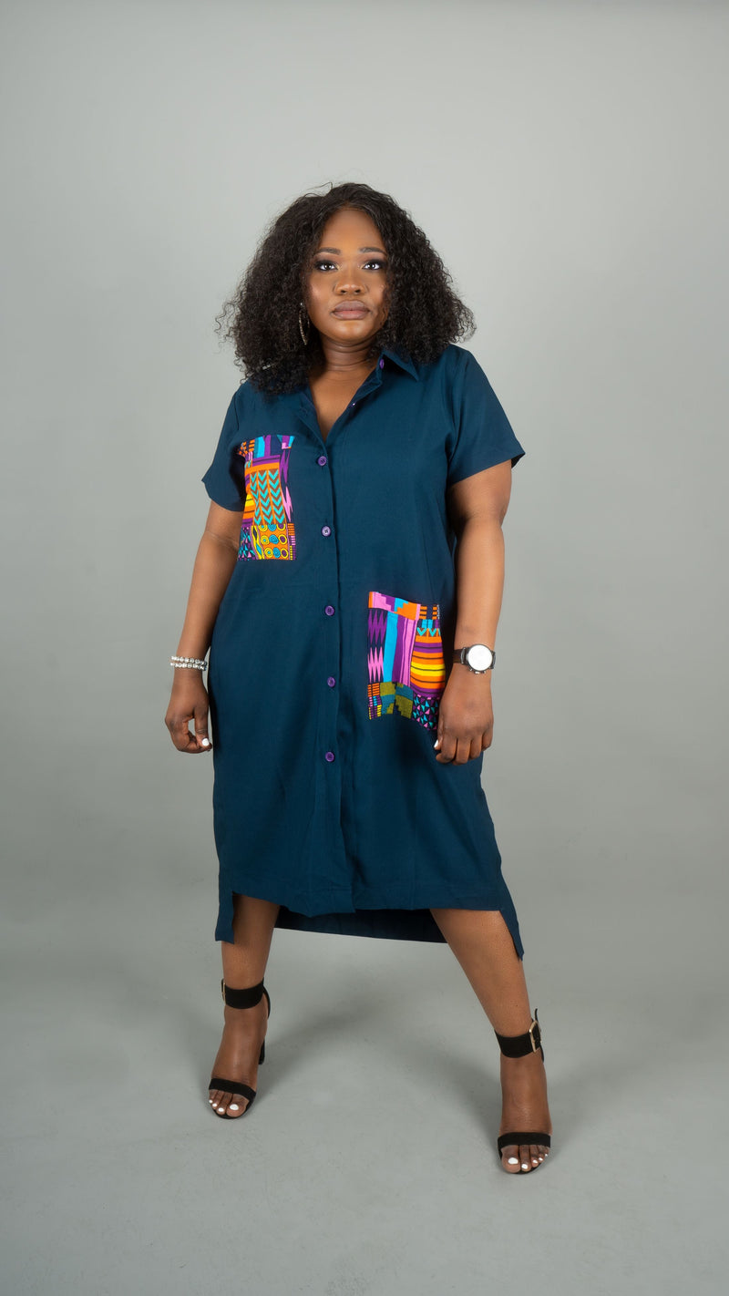 A woman modeling a dark teal button-down shirt dress with colorful geometric patterned pocket details, standing against a solid gray studio background at Bahati Design.